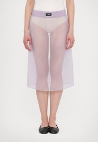 Průhledná lila sukně s elastickým pasem, ke kolenům, vrstvená látka odhalující nohy pod ní, nošena s černými balerínami. Minimalistický design.