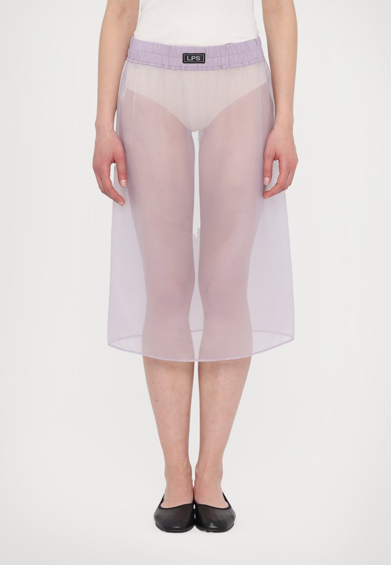 Průhledná lila sukně s elastickým pasem, ke kolenům, vrstvená látka odhalující nohy pod ní, nošena s černými balerínami. Minimalistický design.