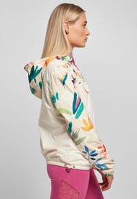 Lightweight, cream-colored jacket with colorful floral print; features a hood, elastic cuffs, and a front pocket. Worn over pink pants.