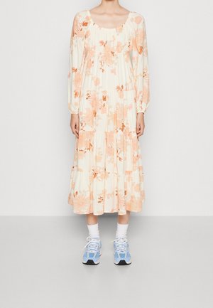 Blumenkleid mit langen Ärmeln und rundem Halsausschnitt, in Creme mit orange und rosa Blumen; kombiniert mit blauen Sportschuhen und weißen Socken.