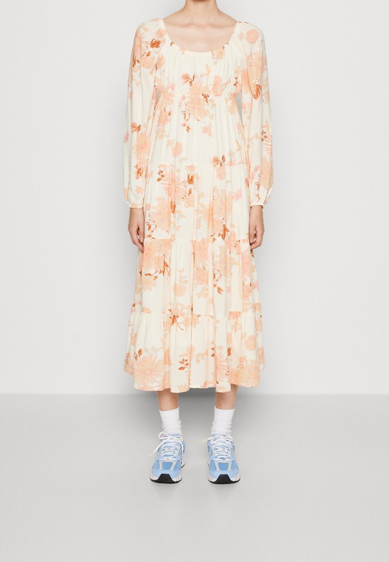 Kwiatowa sukienka z długim rękawem i okrągłym dekoltem, w kolorze kremowym z pomarańczowymi i różowymi kwiatami; zestawiona z niebieskimi butami sportowymi i białymi skarpetkami.