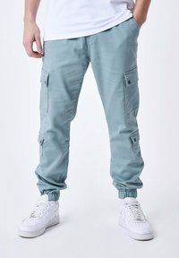 Lichtblauwe cargobroek met elastische boorden en meerdere zijzakken. Gemaakt van stof met een gladde textuur, in een ontspannen pasvorm en met een verstelbare tailleband.