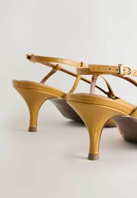 Geltoni aukštakulniais dirželiais puoštos basutės su blizgiu odos paviršiumi, sagties detalėmis ir plonu kulniuku. Tekstūruota paviršiaus dalis su lygiu apdaila.