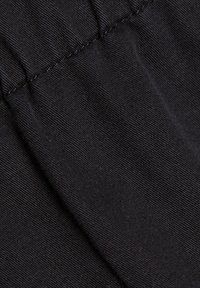 Czarna tkanina o fakturze prążkowanej z marszczonym szwem. Materiał wydaje się miękki i lekki.