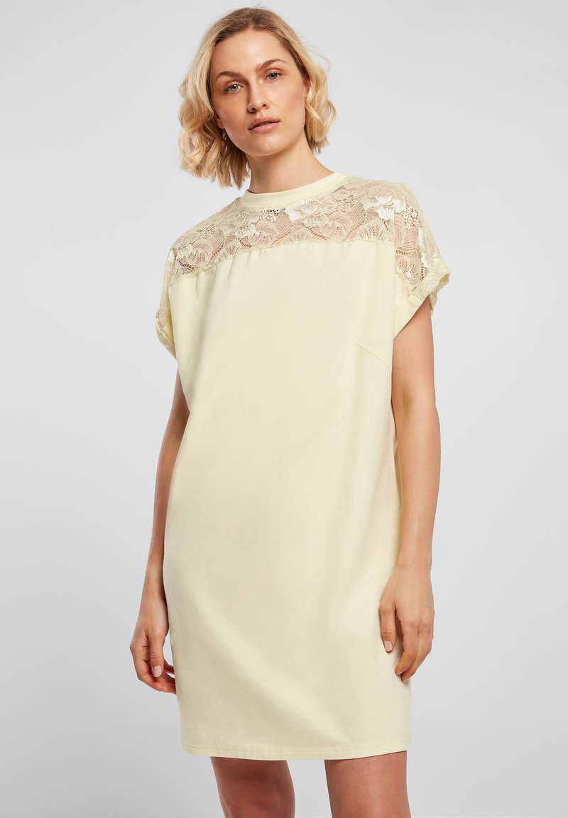 Robe jaune clair avec un empiècement en dentelle, manches courtes et coupe décontractée. Tissu doux avec une texture lisse et un design minimaliste.