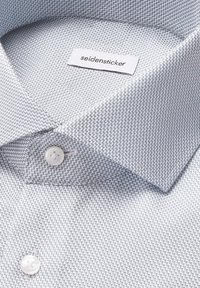 Chemise gris clair avec un motif hachuré de chevrons, dotée d'un col étalé et de boutons blancs. L'étiquette indique "seidensticker."
