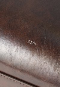 Κοντινή λήψη μιας καφέ δερμάτινης επιφάνειας με ορατή υφή, ραφές και έναν μικρό ανάγλυφο κωδικό "0501" στο κέντρο.