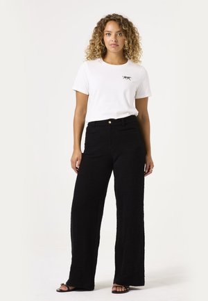 Camiseta blanca de manga corta con un pequeño gráfico de un animal negro, combinada con pantalones anchos de tiro alto y textura negra.