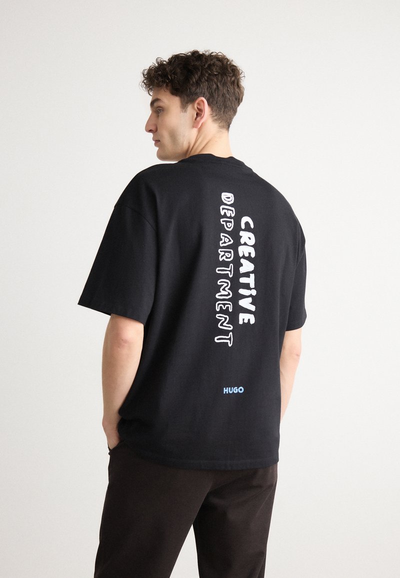 Černé bavlněné tričko s krátkými rukávy, na kterém je vertikální bílý nápis "CREATIVE DEPARTMENT" a modré logo na dolní části zad.