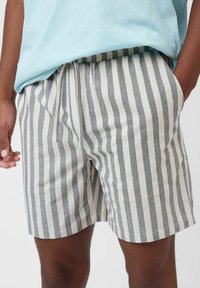 Pantalones cortos a rayas en tejido gris claro y crema, con cinturilla elástica, cordón ajustable y bolsillos laterales, que presentan un ajuste relajado.