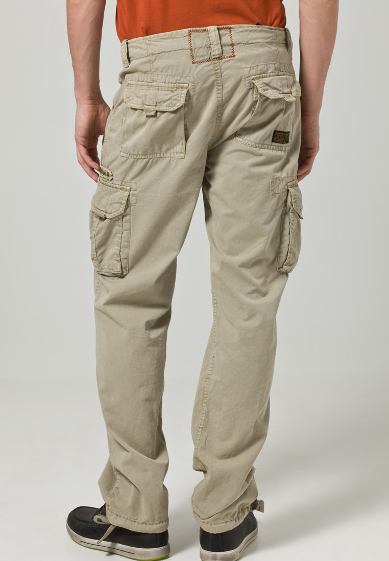 Beżowe spodnie cargo z wieloma bocznymi kieszeniami, elastycznymi mankietami i kontrastującymi czerwonymi szwami w talii. Wykonane z trwałej bawełnianej tkaniny.