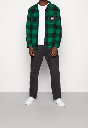 Grøn og sort ternet flannelskjorte med to brystlommer, lagdelt over en hvid T-shirt. Kombineret med mørke bukser og hvide sneakers.