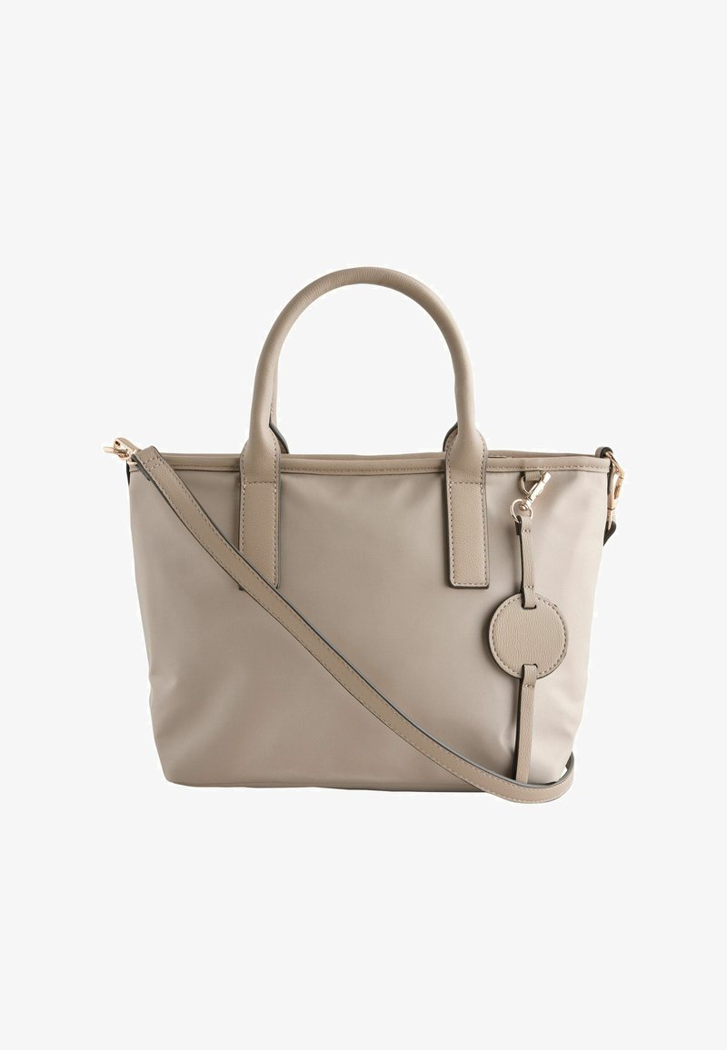 Sac cabas synthétique beige avec double poignées courtes, une bandoulière réglable, des accessoires dorés et une étiquette d'accent circulaire. Texture lisse.