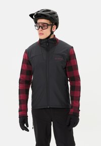 Zwarte en rode geruite jas met een hoge kraag, rits voorkant en contrasterende mouwen. Zwarte handschoenen en een zwarte helm maken de outfit compleet.