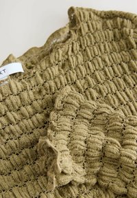 Olijfgroen, gestructureerde stof met een gekreukt patroon, voorzien van een gerimpelde rand. Label zichtbaar met de merknaam nabij de bovenkant.