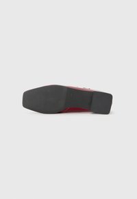 Semelle d'une chaussure de ville rouge avec une semelle avant noire texturée et un talon bloc noir lisse sur un fond blanc uni.