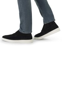 Zwarte suède hoge sneakers met witte rubberen zolen, gedragen met lichtblauwe jeans, vanuit een zijaanzicht terwijl de persoon loopt.