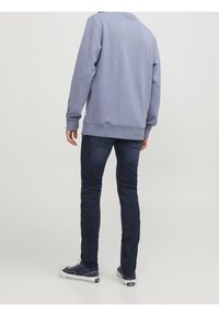 Sudadera azul claro con puños y dobladillo acanalados, combinada con jeans de mezclilla oscura. La persona lleva zapatillas de navidad con suelas blancas.