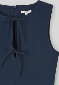 Robe sans manches bleu marine avec une fermeture éclair sur le devant et deux nœuds au niveau du col. Tissu lisse avec un design épuré et sur mesure.