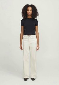 Μαύρο κοντομάνικο πουκάμισο συνδυασμένο με ψηλόμεσα, φαρδιά λευκά παντελόνια. Και τα δύο κομμάτια διαθέτουν καθαρές γραμμές και μινιμαλιστικό σχέδιο.