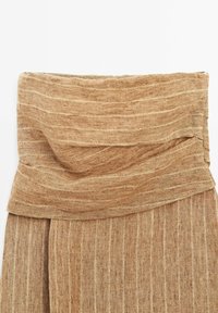 Tissu côtelé beige plié formant une large ceinture sur un vêtement, avec un tricot doux et texturé et un motif à rayures horizontales.