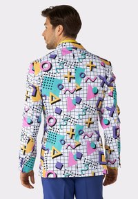 Blazer bianco con motivi geometrici colorati, tra cui triangoli, cerchi e linee in viola, rosa, turchese, giallo e dettagli neri.