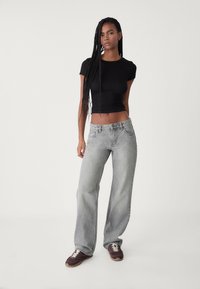 Un haut noir ajusté à manches courtes associé à un jean large gris clair. Les jeans ont un design classique à cinq poches et une finition délavée. Des baskets sombres complètent le look.