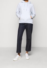 Felpa azzurra con tasca a marsupio, cappuccio con cordino e polsini a coste abbinata a jeans cropped in denim scuri e sneakers bianche.