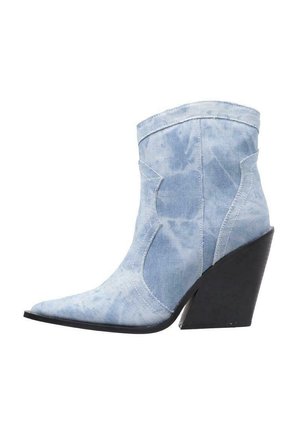 Botín de denim en azul claro con punta afilada, tacón alto negro tipo cuña y costuras decorativas. Textura suave y sin patrones visibles.