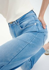 Pantalones vaqueros de denim azul claro con cintura alta, que cuentan con cinco bolsillos, costuras sutiles y un ligero estiramiento para mayor comodidad.