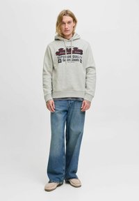Šedá mikina s předním potiskem v tmavě modré a burgundské barvě, doplněná volnými modrými džíny a béžovou obuví. Minimalistický design.