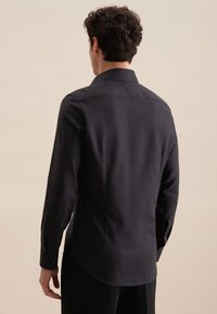 Camicia nera a maniche lunghe con un design strutturato, colletto a punta e polsini con bottoni. Vestibilità su misura con orlo curvo.