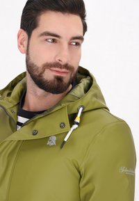 Zielona nylonowa kurtka z dużym kapturem, zamek z przodu, srebrne wykończenie i akcent logo na klatce piersiowej. Posiada kontrastowe sznurki.