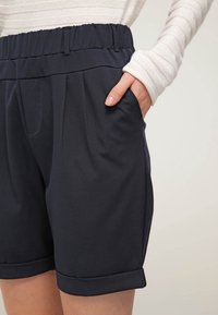 Námořnické modré šortky se širokým elastickým pasem, předními záhyby a bočními kapsami. Lem je ohrnutý pro uvolněný vzhled.