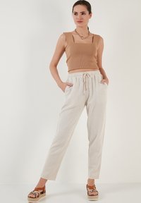 Beige geribbelde crop top met vierkante halslijn, gecombineerd met lichtbeige broek met aantrekkoord. Model draagt bruine sandalen met textuuraccenten.