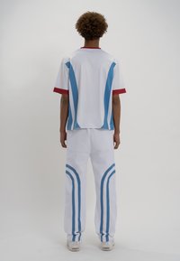 Balti sporta apģērbs, kas sastāv no īsām piedurknēm tērpta krekla ar sarkaniem akcentiem un zilām svītrām, pārī ar baltām biksēm ar zilām sānu svītrām.