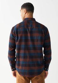 Koszula z długim rękawem w niebiesko-brązowo-czarną kratę; wykonana z miękkiego materiału, z mankietami na guziki i zakrzywionym dołem. Widok od tyłu.