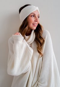 White knit sweater with a high, ribbed cowl neck and oversized sleeves. Accompanied by a matching knitted headband with a twisted design.