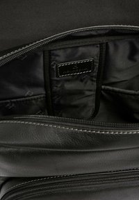 Interno di una borsa in pelle nera, dotato di un comparto zip, texture liscia e un'etichetta. Fodera in tessuto scuro con tasche per l'organizzazione.