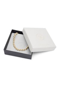 Gold bead necklace resting in a gray suede box within a black presentation box; smooth texture and spherical bead design.