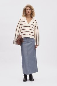 Pull en tricot crème avec des rayures horizontales marron, décolleté en V profond et manches larges. Associé à une jupe maxi en denim bleu et des bottines noires.