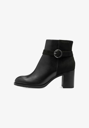 Bottine en cuir noir avec un bout rond, une bande en suède et une boucle métallique circulaire. Talon épais pour plus de stabilité.