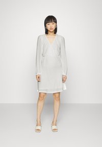 Vestido envolvente branco, texturizado, com mangas longas e decote em V, apresentando uma cintura ajustada e uma barra logo acima dos joelhos. Tecido suave.