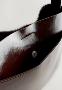 Pruun nahast kotti sisu on sileda ja läikiva tekstuuriga, millel on hõbedane nööp-kinniti ja peen õmbluse detail.