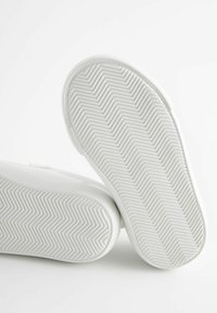 Hvide sneakers med en glat overdel og en gummisål med et fiskebensmønster. Designet er minimalistisk uden synlige accenter.
