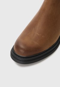 Braune Lederstiefel mit runder Zehenform, ausgestattet mit einer glatten Oberfläche und einer schwarzen Gummisohle. Das Design weist dezente Farbvariationen auf.