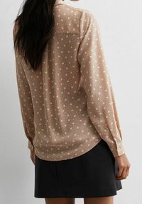 Långärmad beige blus med små hjärtan, genomskinligt tyg, knappade manschetter och något rundad nederkant. Matchad med en svart kjol.