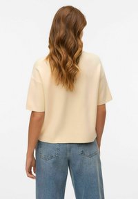 Kortärmad krämfärgad topp med en avslappnad passform, tillverkad av mjukt tyg. Matchas med ljusblå högmidjade jeans av denim, med bakfickor.