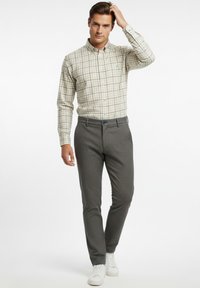 Camisa de cuadros en beige y verde oscuro, estilo abotonado, combinada con pantalones grises texturizados. La modelo lleva zapatillas blancas.