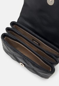 Portefeuille en cuir noir matelassé ouvert montrant trois compartiments beiges doublés de tissu et une fermeture pression dorée sur le rabat.